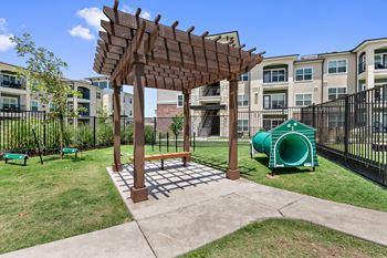 A wooden pergola with a bench is in the middle of a playground.